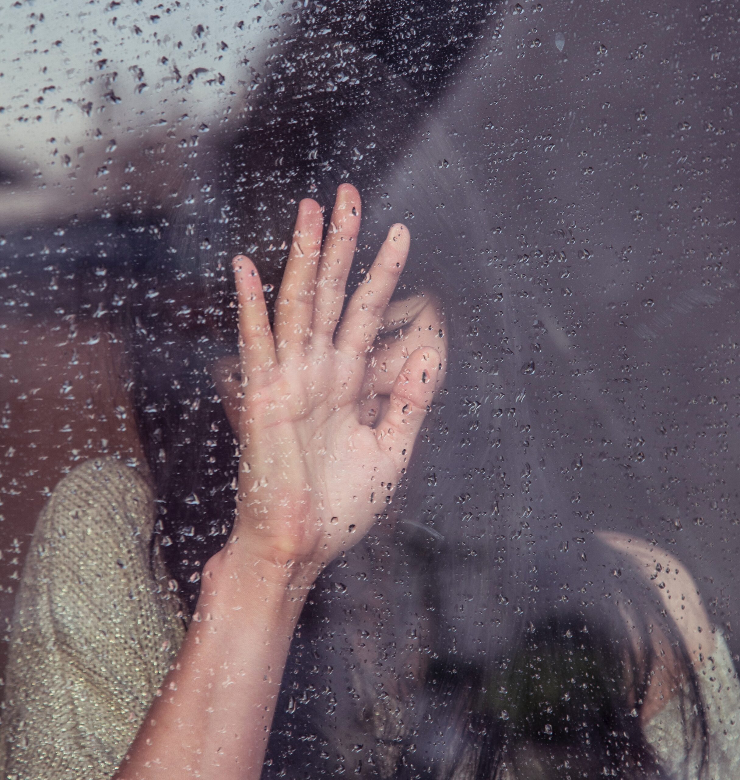 a woman standing behind a window covered in rain