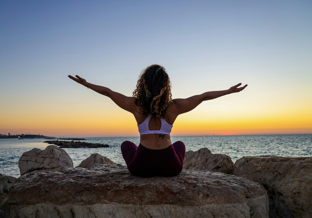 a woman sitting on top of a rock near the ocean