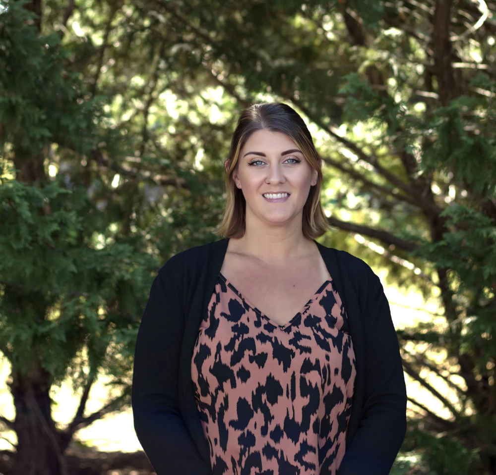 a woman named Ashly Lupinacci standing in front of a bush