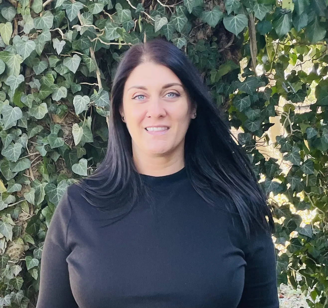 a woman named Ashly Lupinacci standing in front of a bush