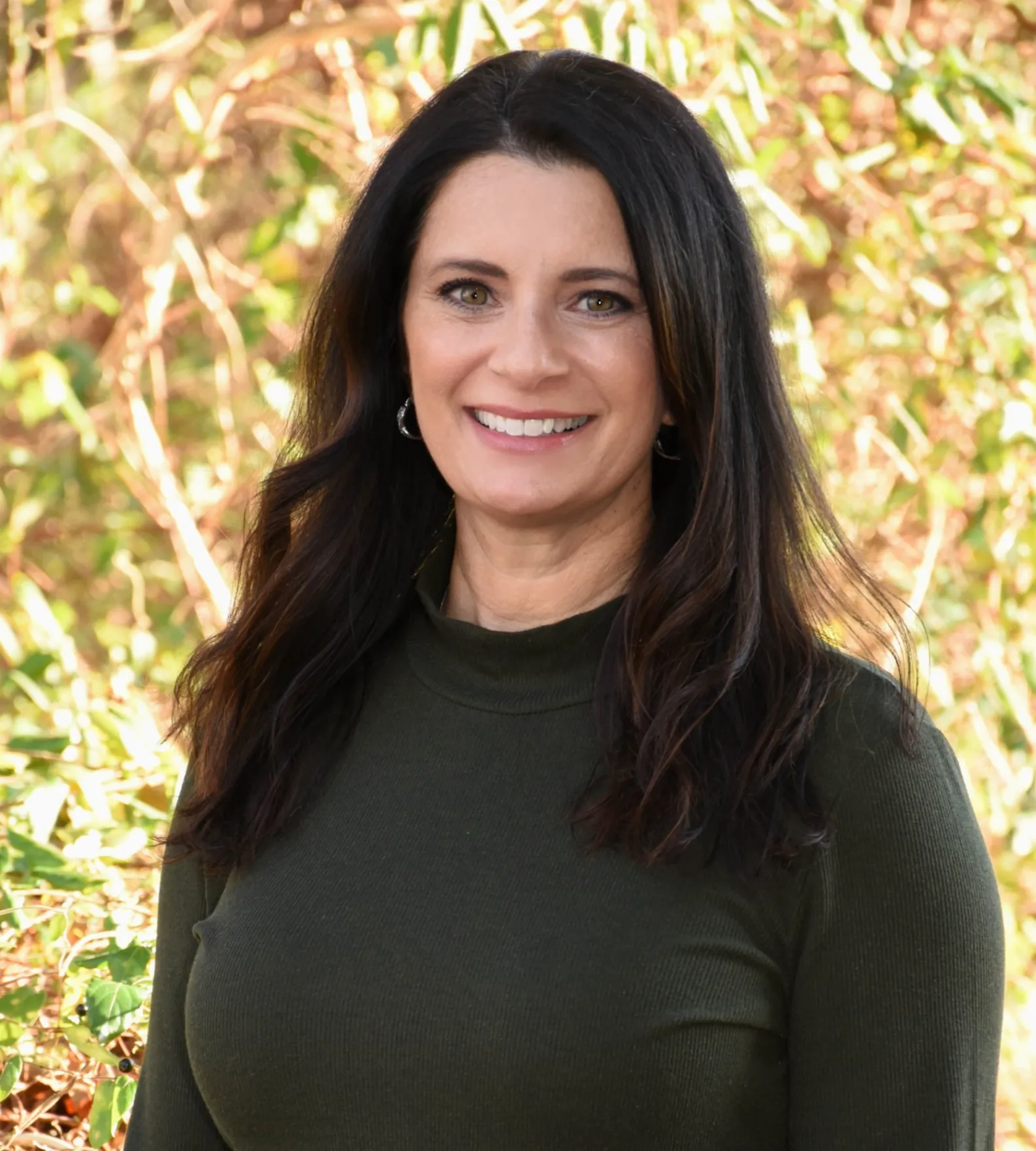 a woman named Michelle Leyman in a green shirt standing in front of a bush