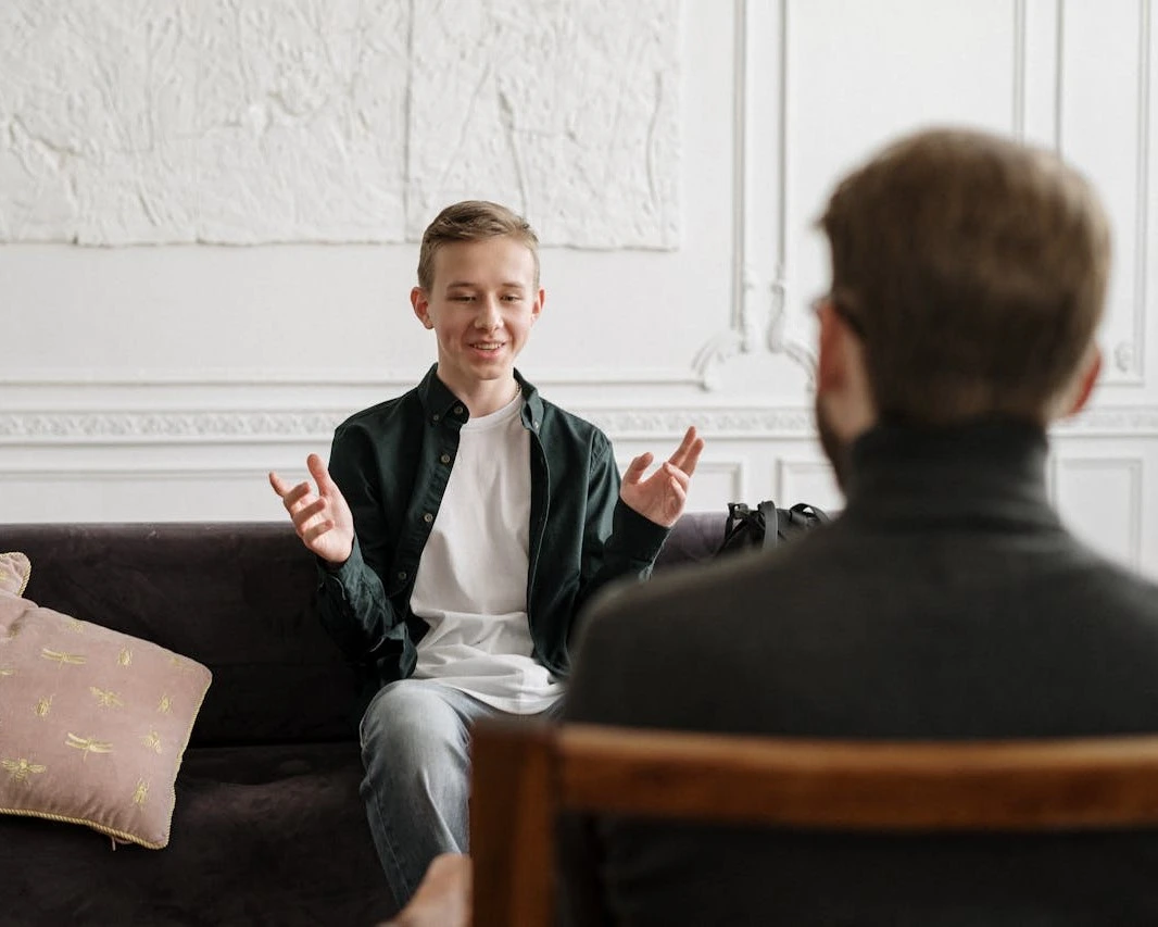 a teenage kid sitting on a couch talking to another man