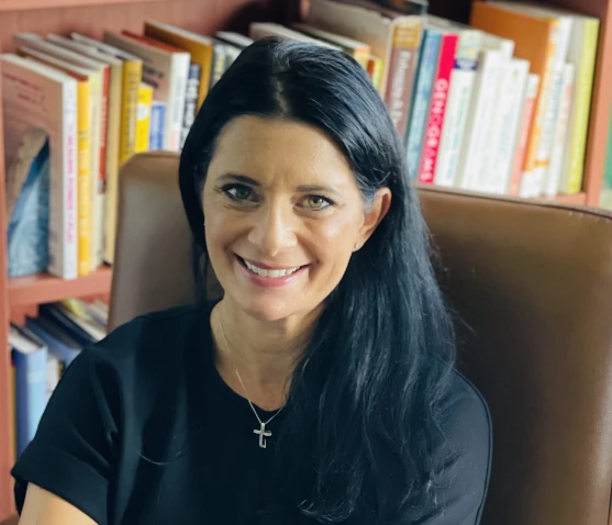 a woman smiling with a bookshelf on the back