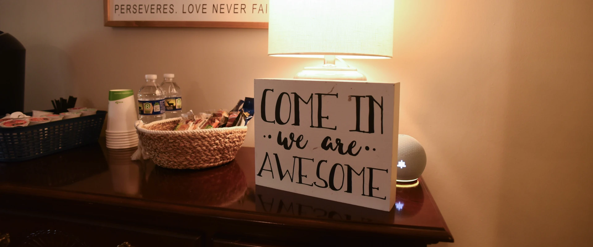 a photo of a desk with lit lamp and a signage saying come in we are awesome